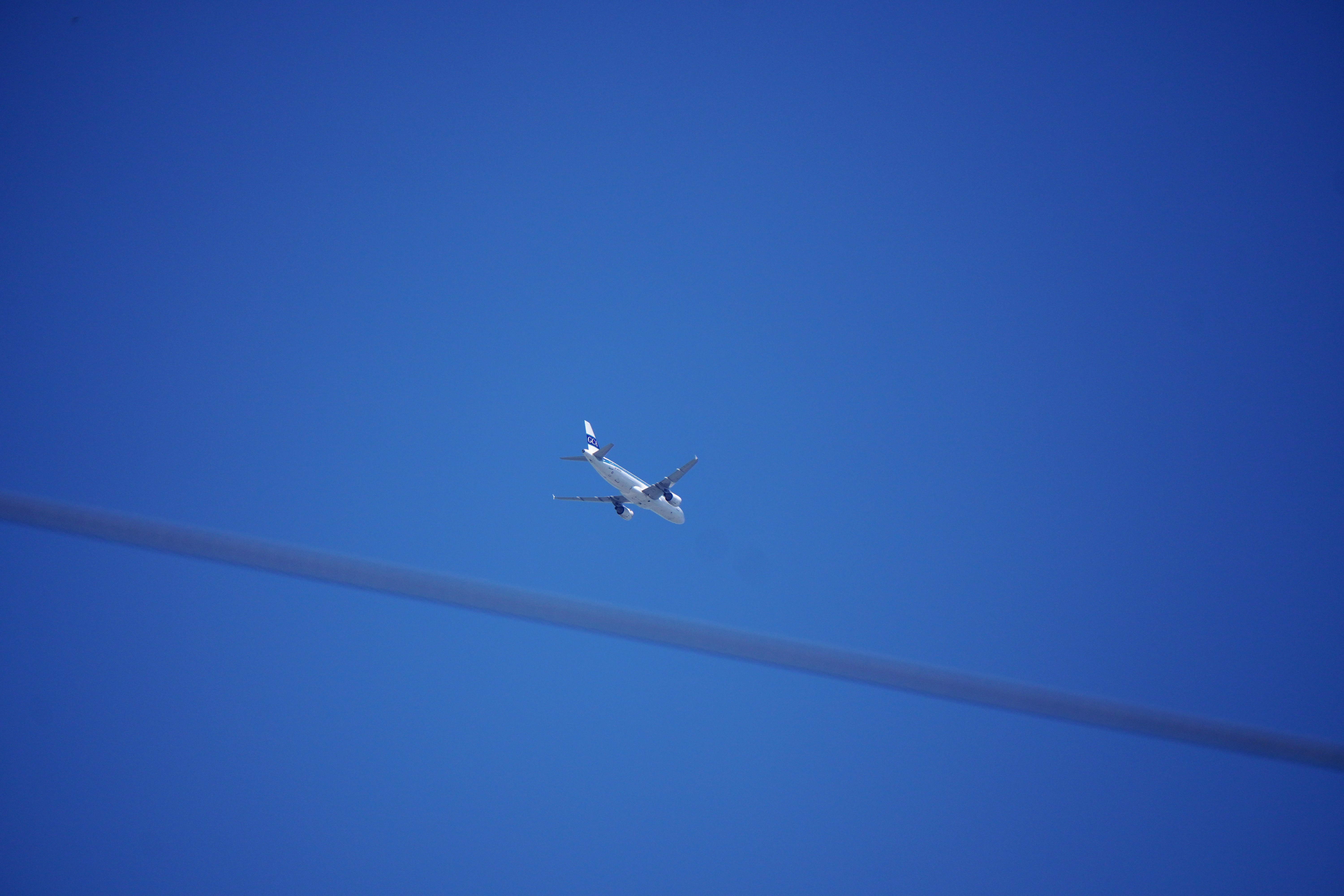 A leased airplane used by ICE to transport immigrants in a blue sky. A power line runs through the bottom portion of the screen.