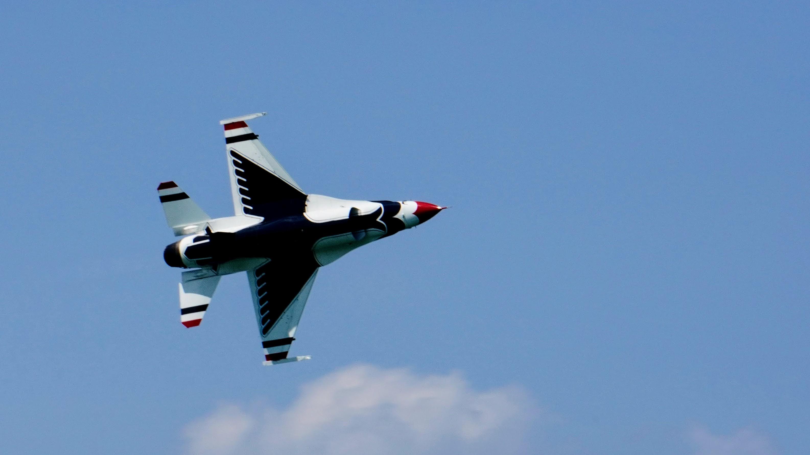 A US Air Force Thunderbirds jet flies over a crowd watching the Gary Air Show 2025. There is is a silhouette of a thunderbird on the jet's fuselage.