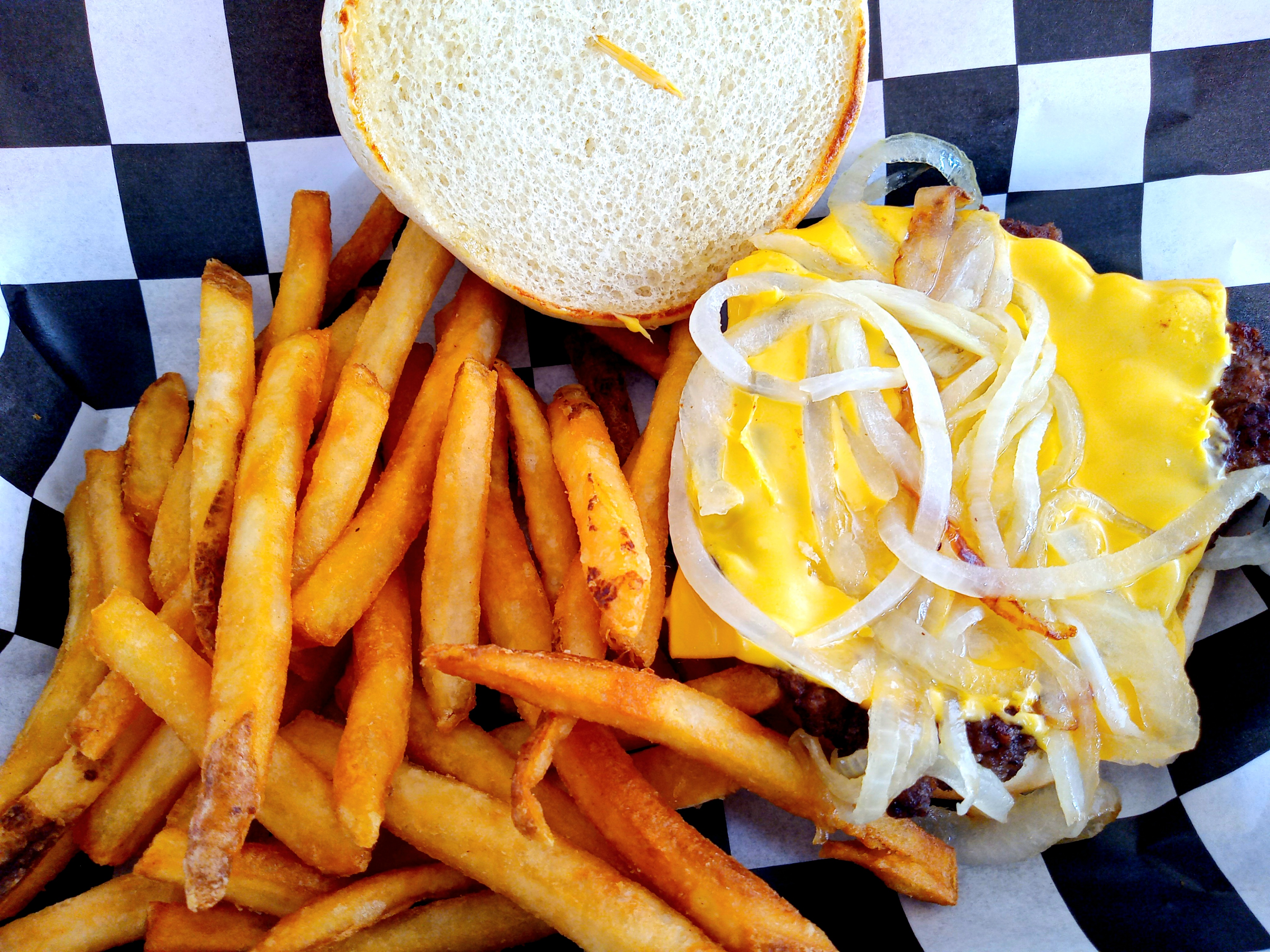 A cheese burger with onions and fries on black and white checkerboard wax paper.